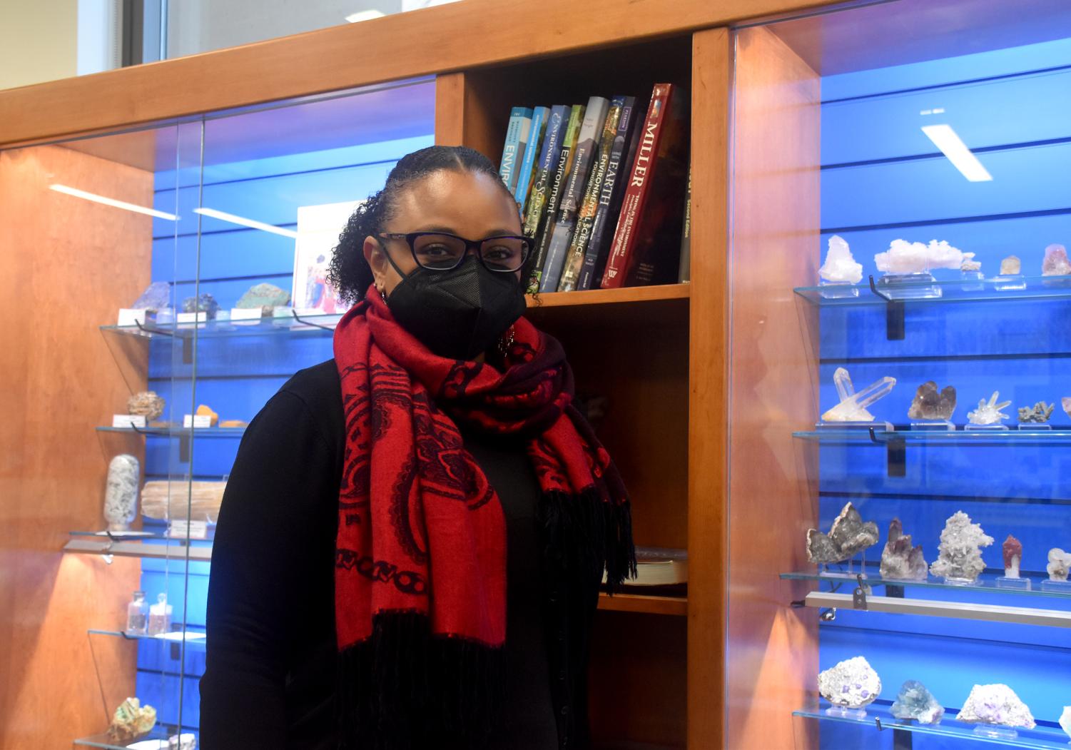 Dr. Danielle Andrews-Brown stands in front of minerals on display in the department of Geology and Environmental Science