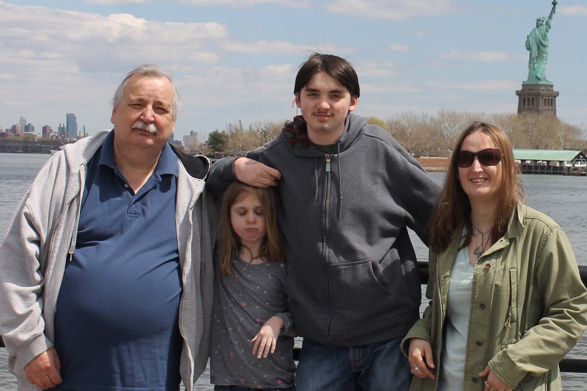 Four people pose in front of the Statue of Liberty.