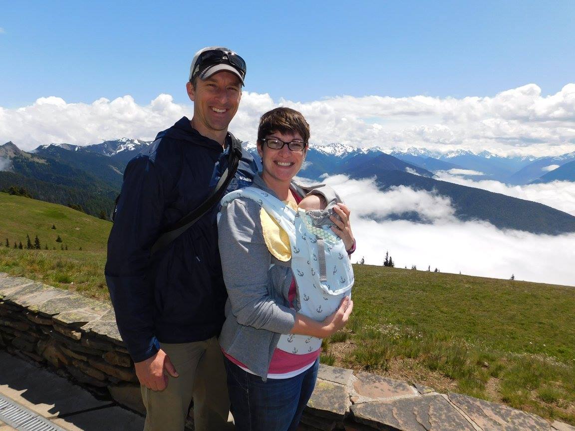 Family of three stands in front of Hurricane Ridge mountain range.